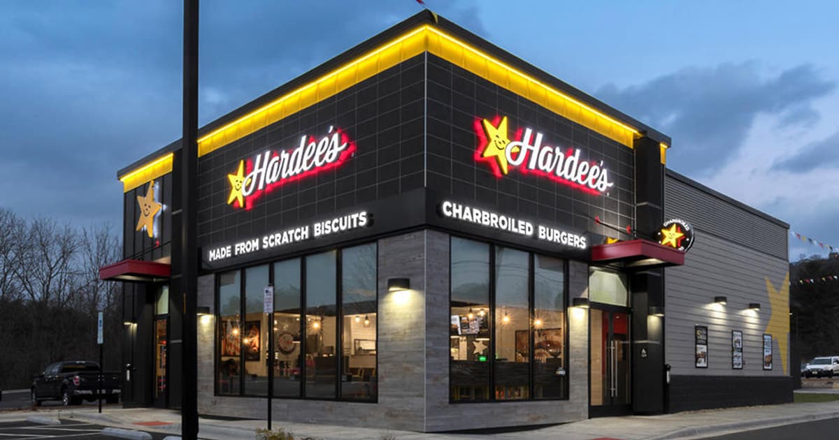 A Hardees restaurant at dusk, with illuminated signage and yellow trim, featuring Made from Scratch Biscuits and Charbroiled Burgers on the exterior.