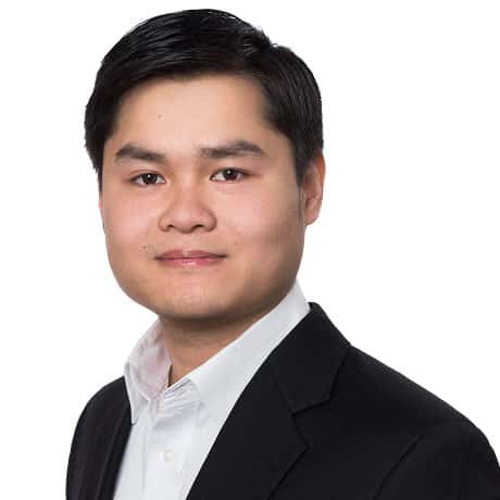 A man with short black hair wearing a black suit jacket and white dress shirt, posing for a professional headshot against a plain white background.