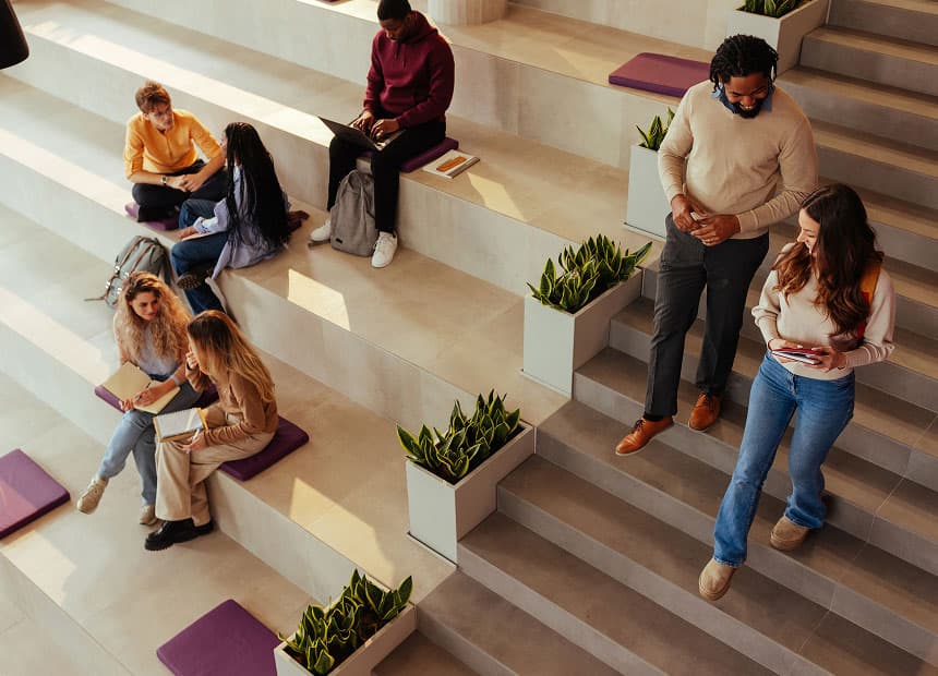 Several people sit and walk on wide, tiered steps with potted plants and cushions, talking and using laptops in a modern, indoor space. FPO is overlaid in pink text.
