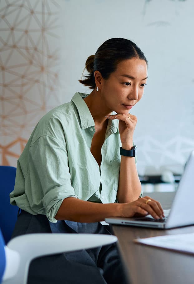 A woman sits at a desk, looking thoughtfully at her laptop. She rests her chin on her hand. The letters FPO are overlaid in pink. The background is a modern office space.